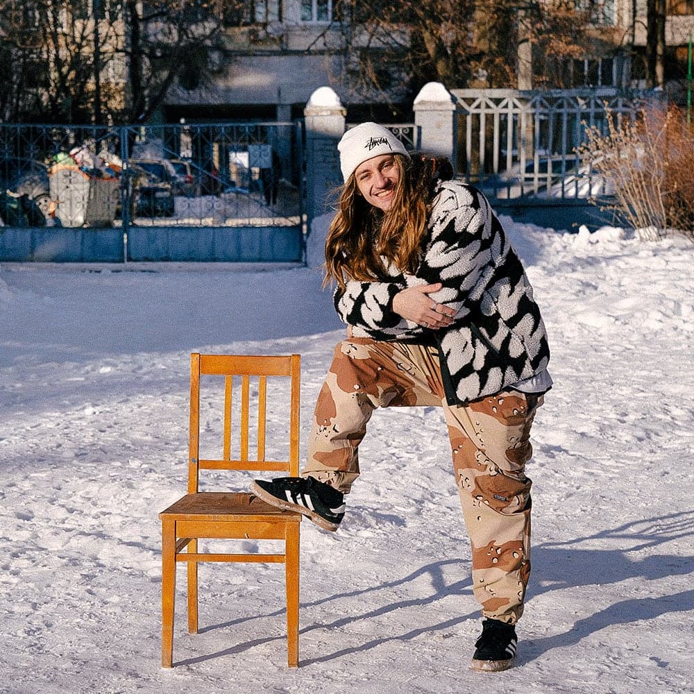 Yurii Korotun stretching a leg on a wooden chair in a snow-covered courtyard