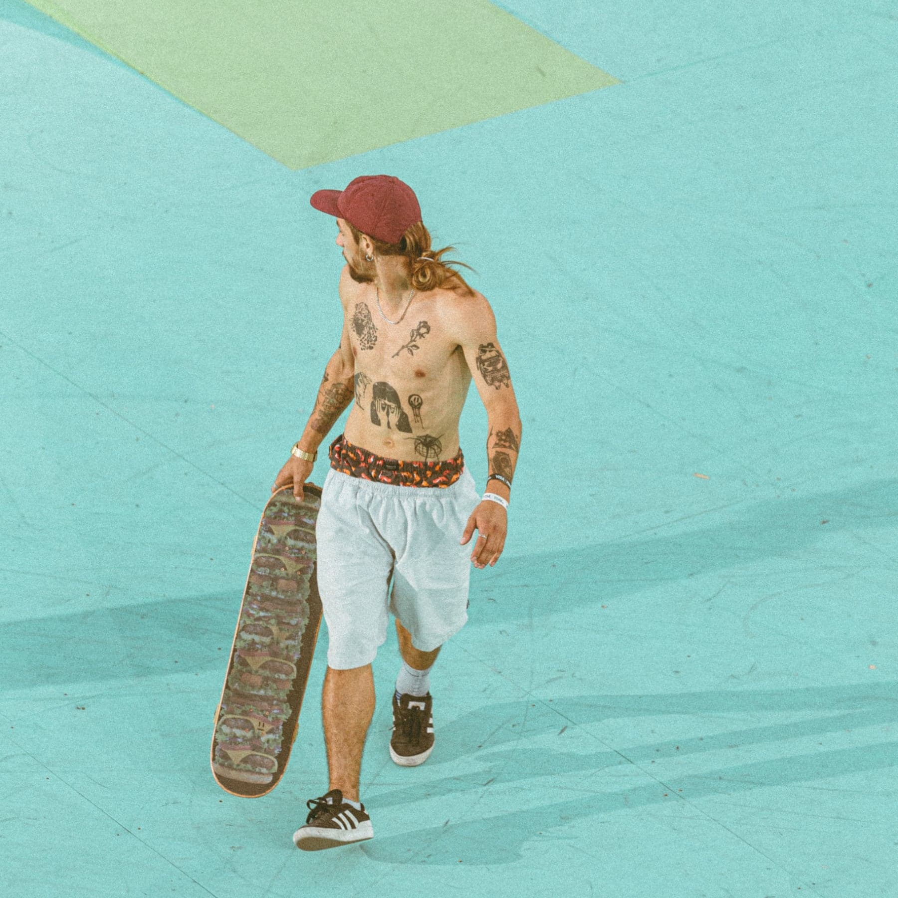 Skateboarder crossing the turquoise flat of a skatepark with a deck in hand