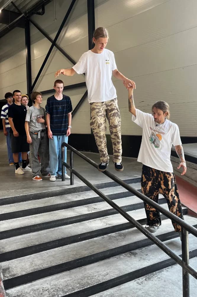 Coach steadying a camper by the hand as he rides the handrail down an indoor set of stairs