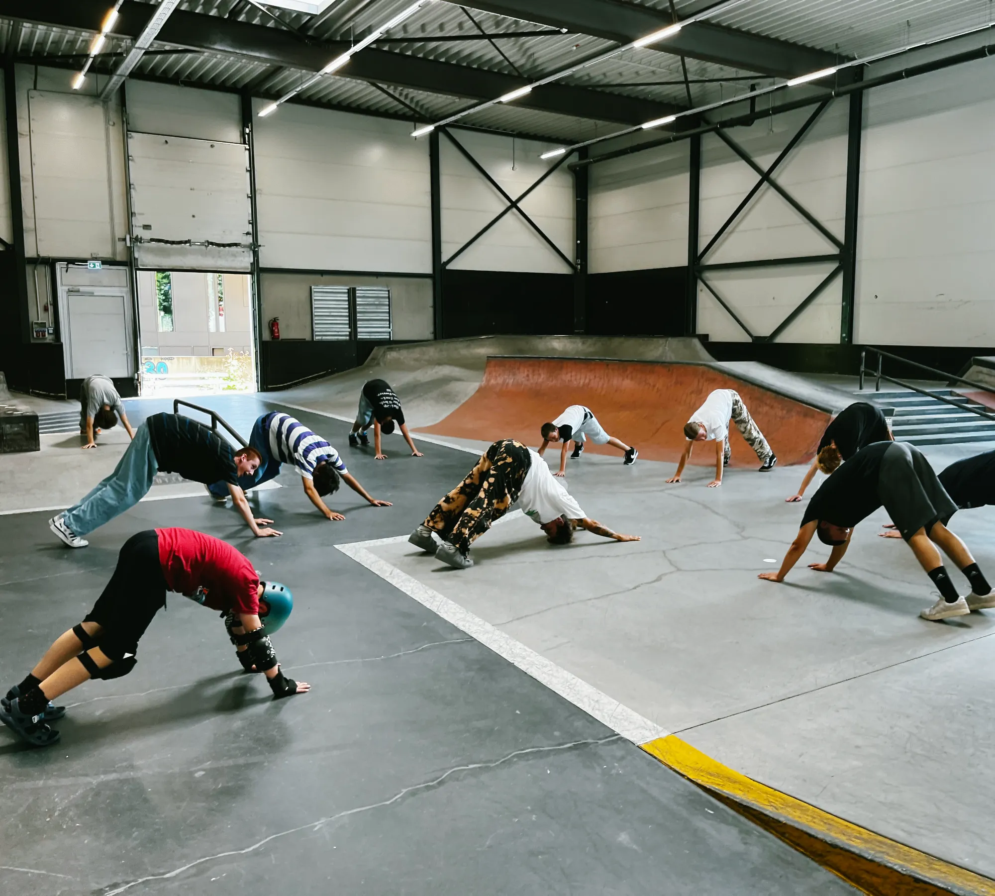 Campers and coaches stretching together on the flat before a session at the indoor skatepark
