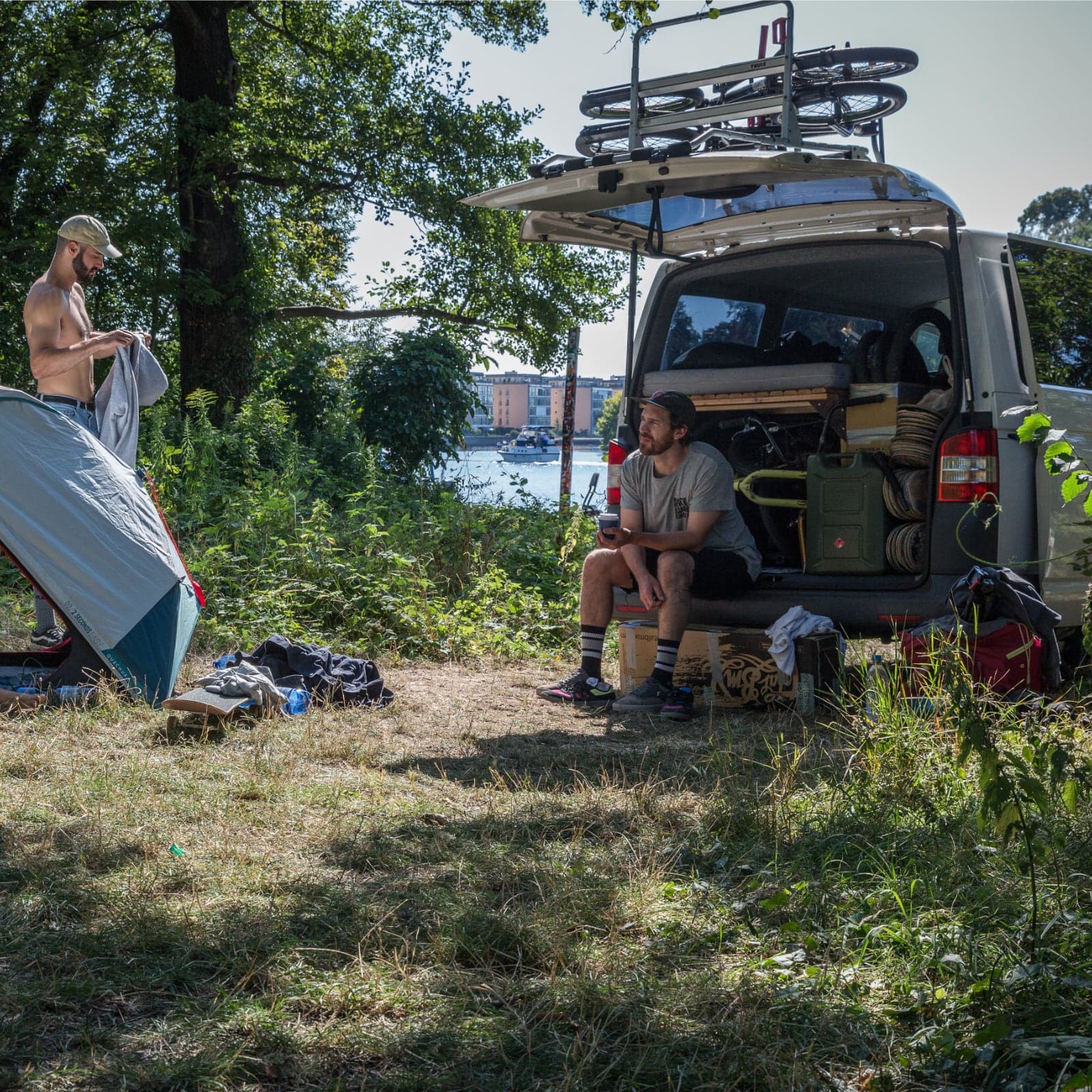Overnight camp beside a river with a tent pitched next to the loaded convoy van