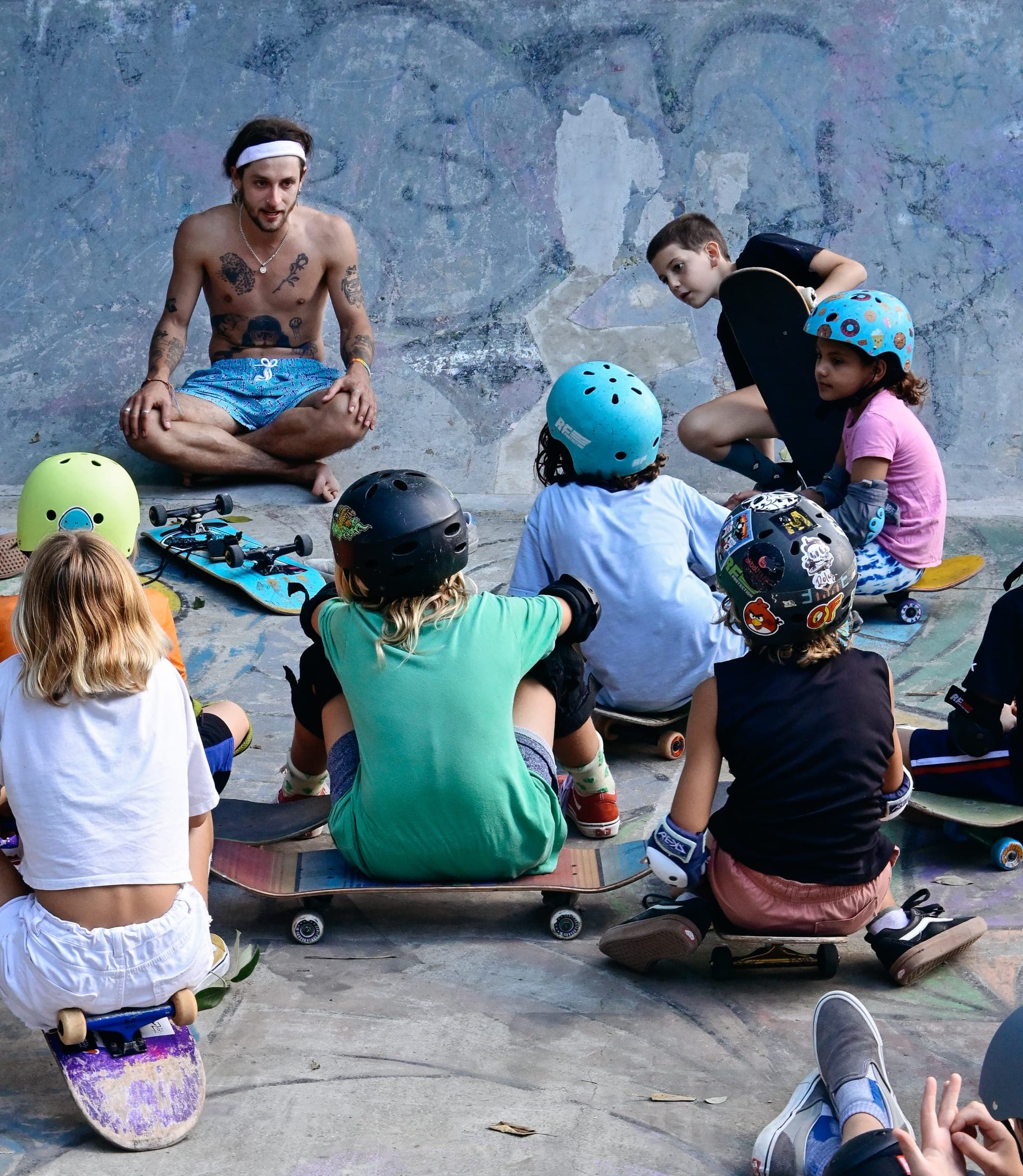 Coach sitting with a circle of helmeted kids during a skate camp session in a concrete bowl