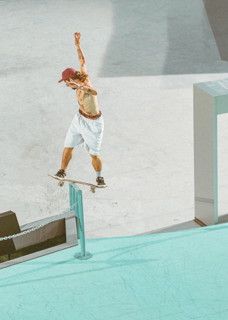 Skateboarder boardsliding a turquoise handrail at a concrete skatepark