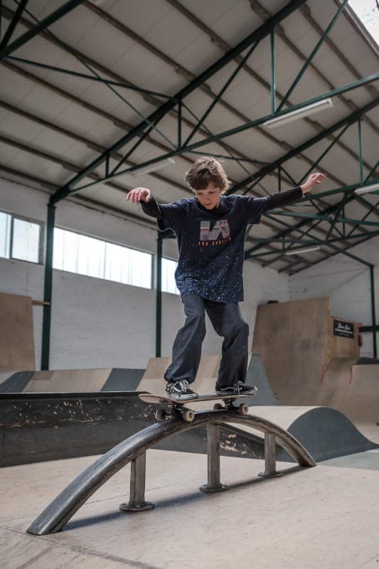 Young skater balancing along a curved rail at the indoor skatepark