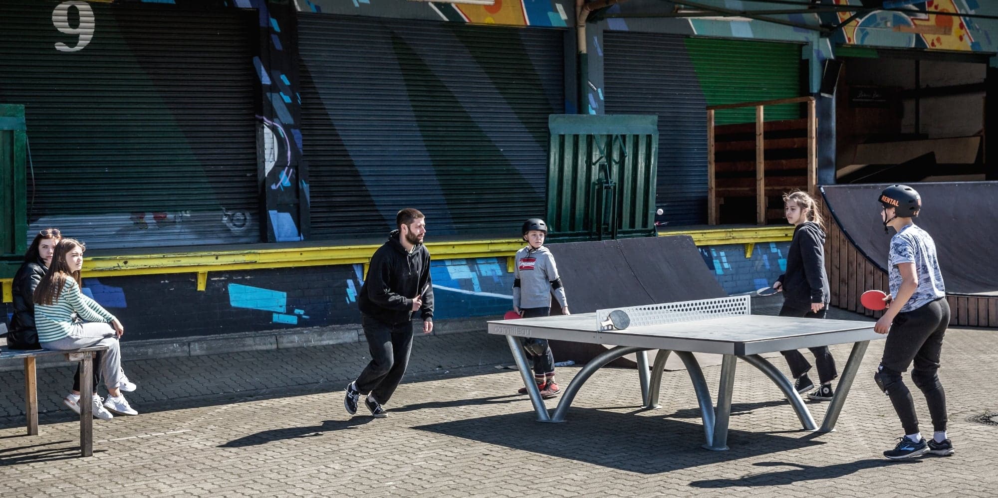 Students and coaches playing table tennis beside the ramps between skate sessions