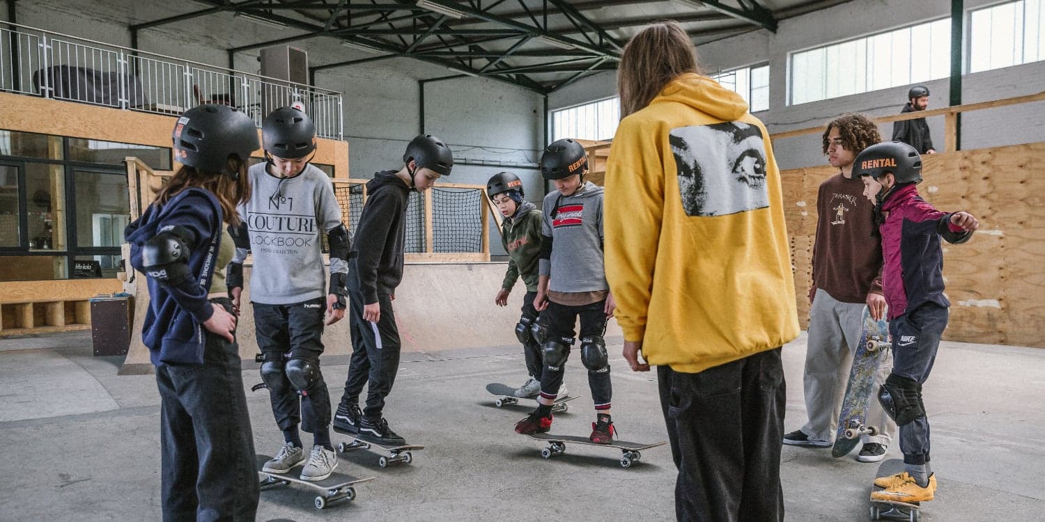 Coach leading a line of helmeted children through balance basics at an indoor skatepark