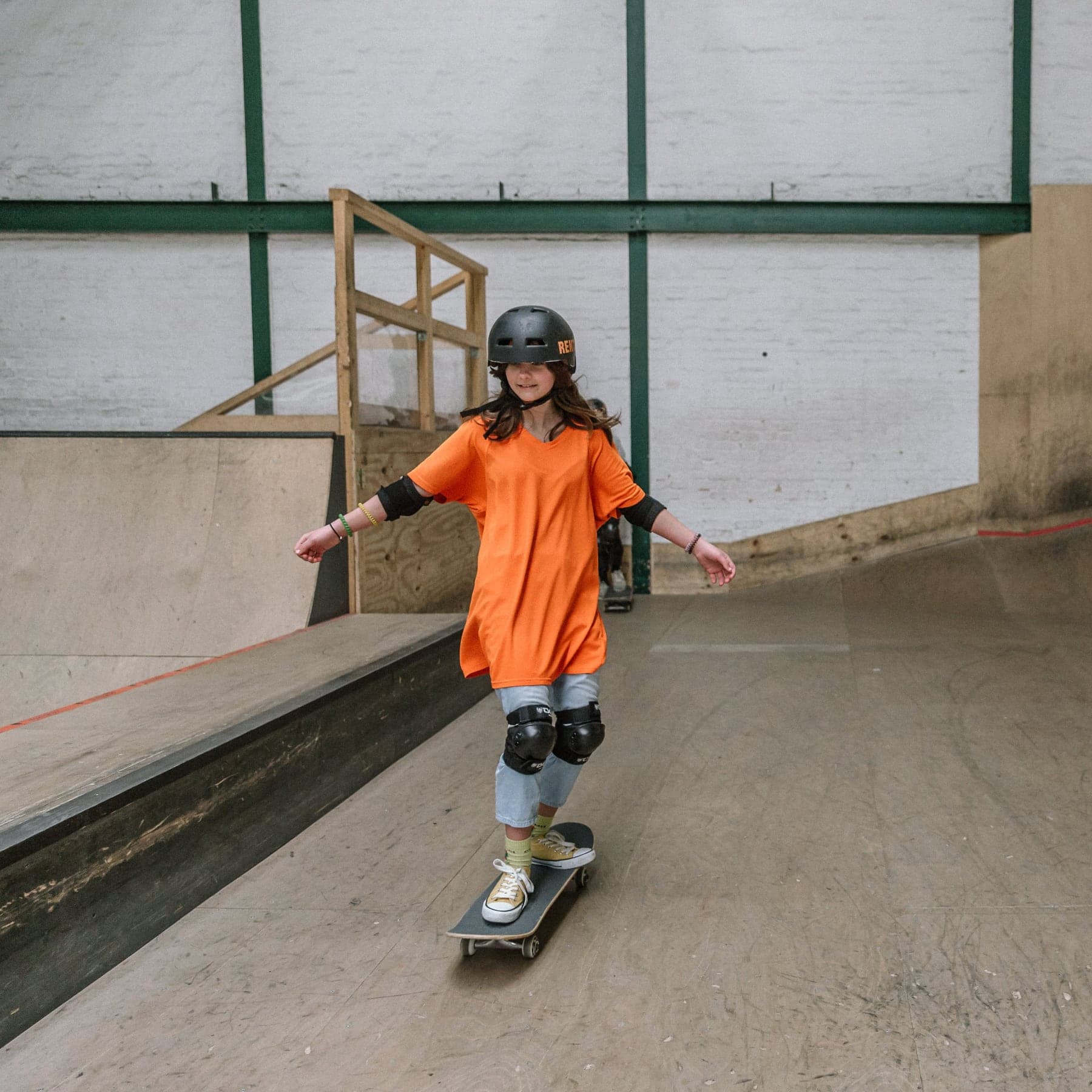 Young skateboarder in a helmet and knee pads rolling across an indoor skatepark