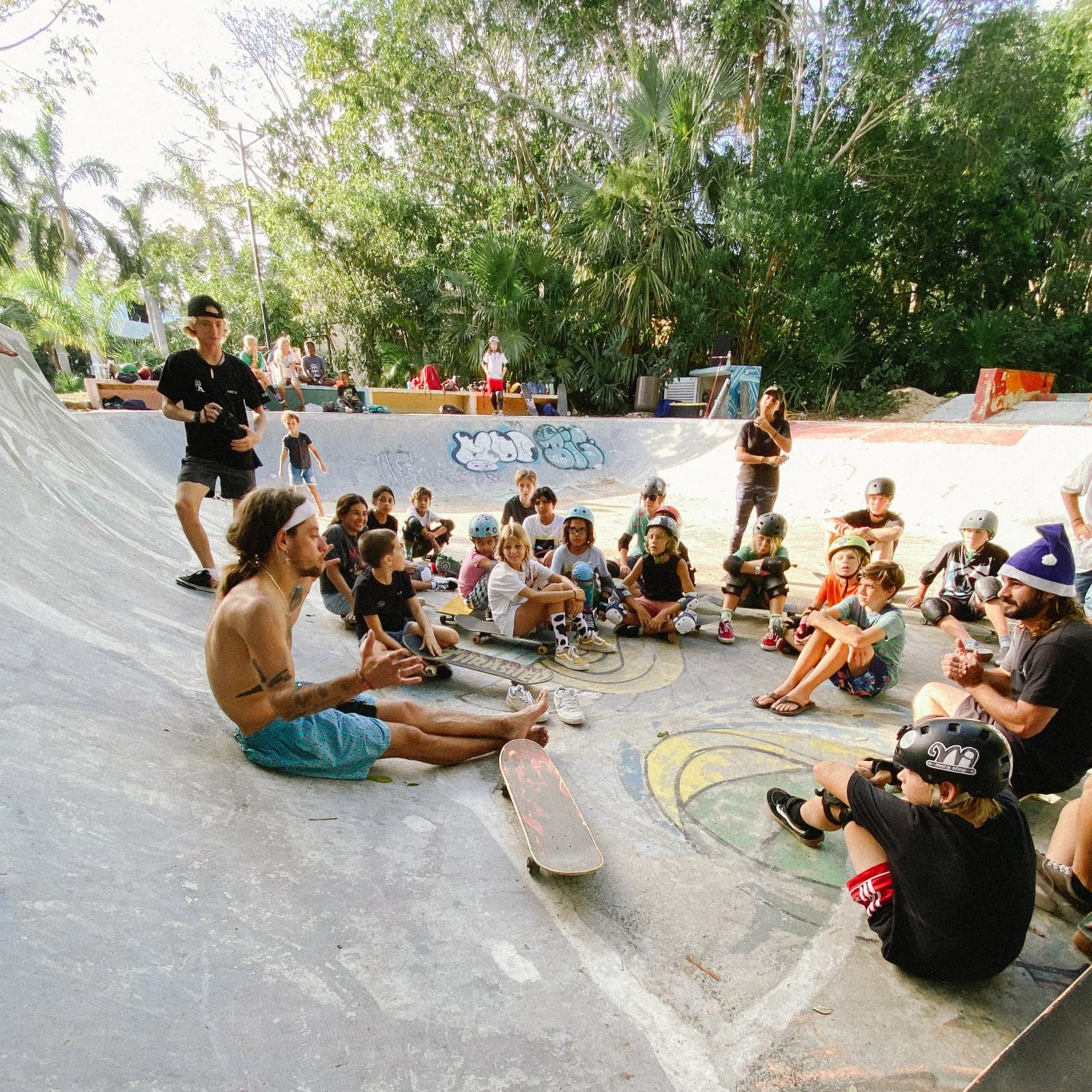Coach talking through the session with a circle of kids sitting in a concrete bowl at an outdoor skate camp